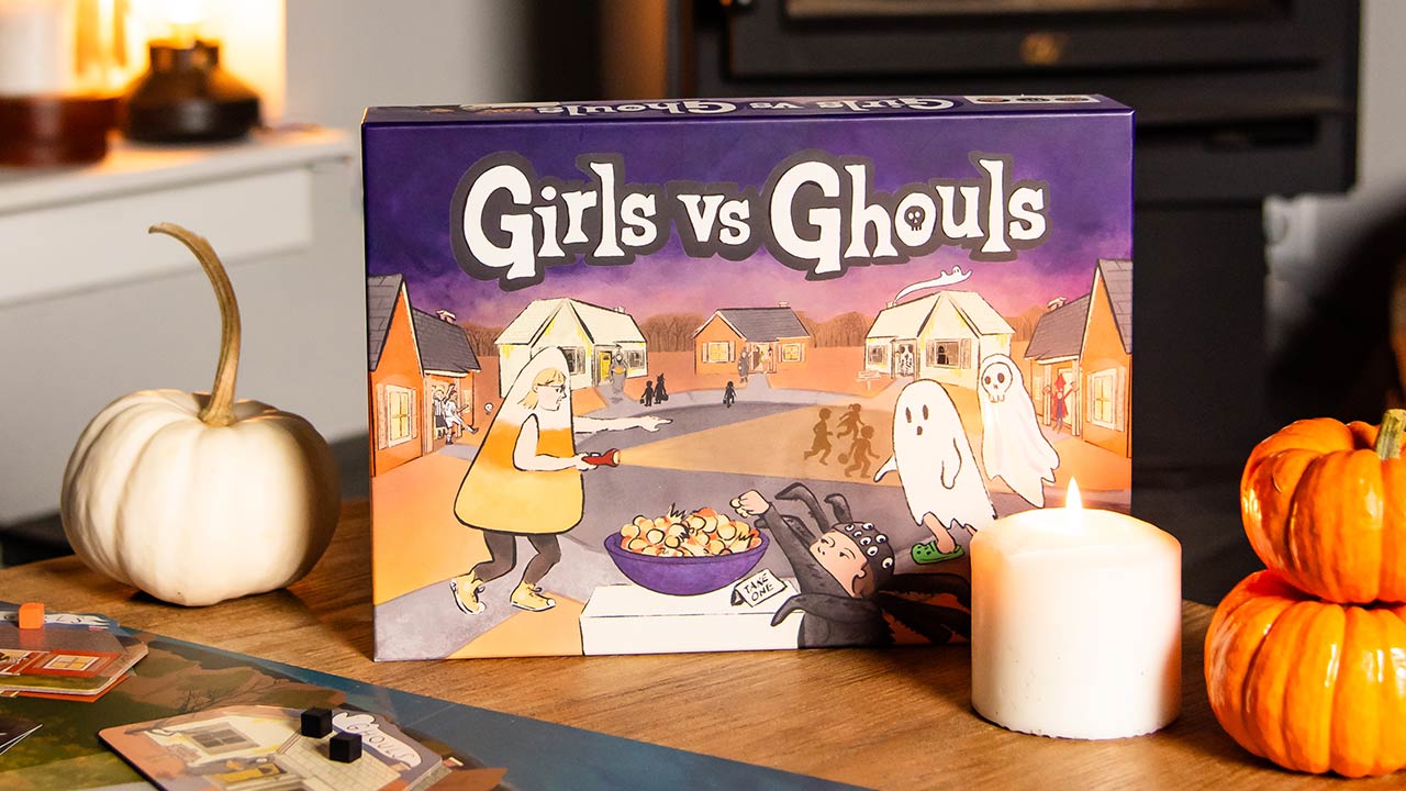 Halloween themed board game 'Girls vs Ghouls' on a table with pumpkins and a candle.